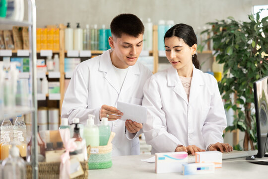 Two male and female pharmacists attentively stocktaking medicines with computer at small pharmacy shop