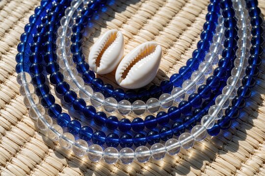 Blue, clear bead necklace with white cowrie shells on straw mat. Traditional Yoruba religious jewelry for Yemaya orisha. Afro Cuban spiritual accessory for ritual, meditation, cultural celebration.