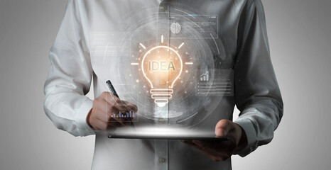 A businessman uses a tablet to write down ideas while a digital light bulb graphic symbolizes his innovative thinking in technology and creativity for future projects. Nascent © InfiniteFlow