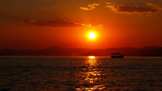 Fishing boat sailing under red sun. Fishing boats sailing with people on waves by burning skyline in evening