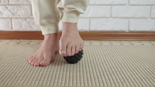 Man massaging his foot with a spiky ball for pain relief. Close-up of a man's bare feet rolling a spiky massage ball on the floor to relieve plantar fasciitis pain, improve circulation