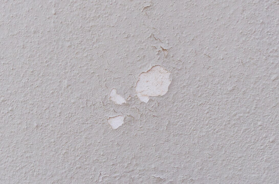 Peeling paint on a porous grey building wall.