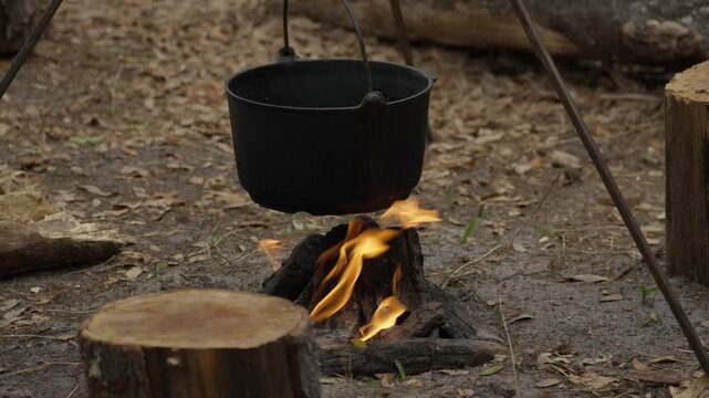 Bright flames heat a cast-iron pot on a tripod over a forest campfire. Tourist camping. Outdoor cooking. Ecotourism recreation..