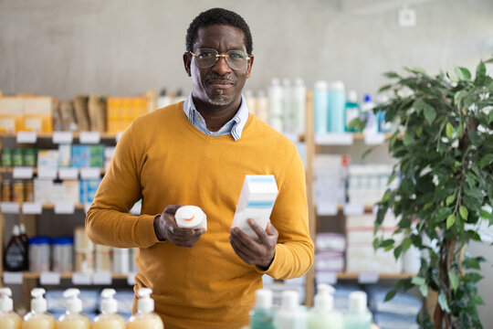 Male buyer in glasses attentively chooses skin cream at the drugstore