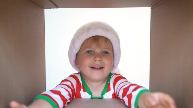 Happy child is unpacking a Christmas gift box. Kid dressed in Xmas pajamas is having fun at home. Slow motion