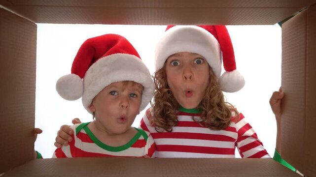 Happy children are unpacking a Christmas gift box. Kids dressed in Xmas pajamas are having fun at home. Slow motion