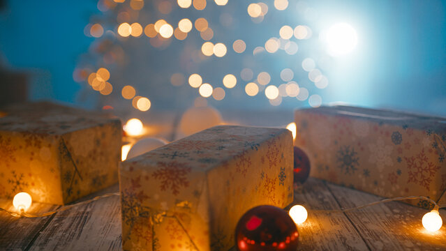 A man hand arranges Christmas presents on the table in front of the tree