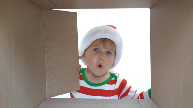 Happy child is unpacking a Christmas gift box. Kid dressed in Xmas pajamas is having fun at home. Slow motion