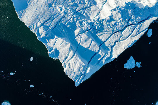 Aerial view of Ilulissat glacier featuring deep crevasses and intricate ice textures floating in the dark waters of Greenland.