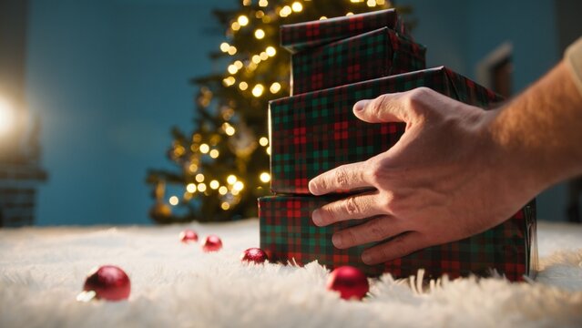 Hand Delivers First Christmas Gifts On A White Carpet In Front Of Glowing Tree