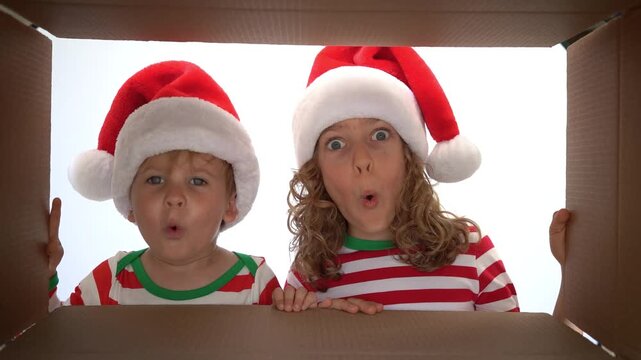 Happy children are unpacking a Christmas gift box. Kids dressed in Xmas pajamas are having fun at home. Slow motion