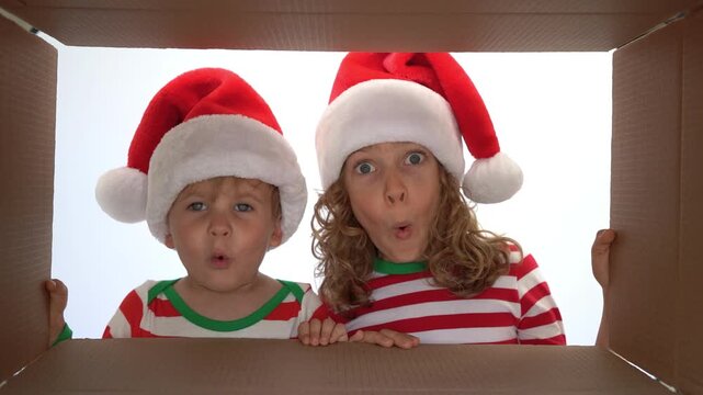 Happy children are unpacking a Christmas gift box. Kids dressed in Xmas pajamas are having fun at home. Slow motion
