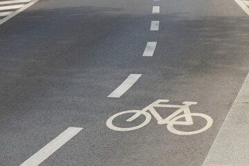 Obraz premium White bicycle lane symbol and dashed road markings on smooth asphalt beside concrete curb, viewed from above as urban transportation infrastructure in a dedicated cycling lane