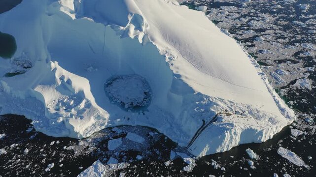 Aerial view of Ilulissat glacier showing ice textures and meltwater pools surrounded by floating icebergs in the arctic waters of Greenland.