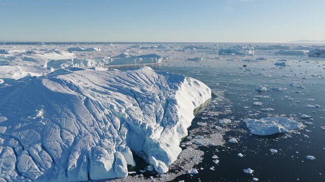 Aerial view of Ilulissat glacier with massive icebergs floating in the dark arctic waters of Greenland.