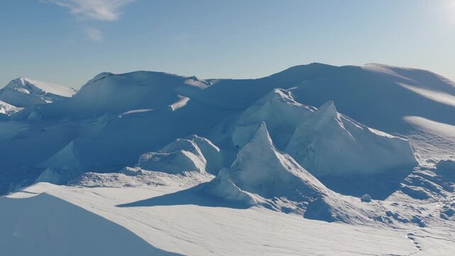 Aerial view of the massive Ilulissat glacier with jagged ice formations and snow-covered landscape under a clear blue sky in Greenland.