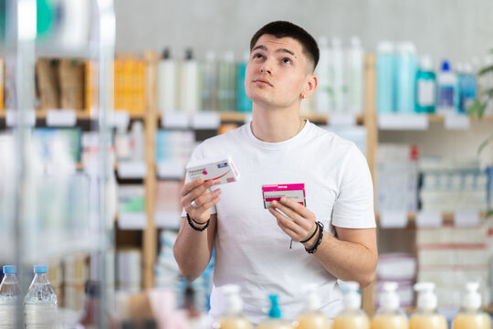 Young man buys paracetamol at pharmacy and compare with other medicine, carefully reads patient information, checks composition of drug. Checks for absence of harmful substances, view product in
