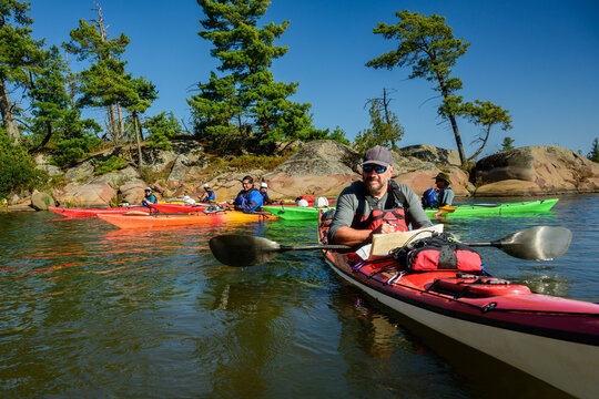 Sea kayaker writes in a notebook on his kayak deck as a paddling group rafts up by a pine island on Georgian Bay, Ontario, Canada