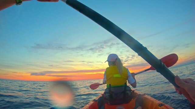 A woman in a vibrant yellow life vest paddles through the tranquil waters at sunset, embracing an adventurous sea kayaking experience.