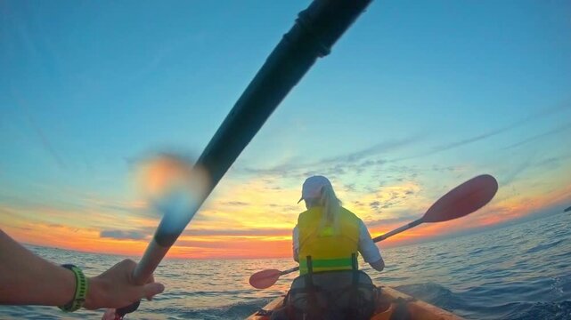 The young couple paddles in sync, embracing their sea kayaking adventure under the vibrant sunset, active lifestyle and recreational pursuit evident in their shared smiles and steady strokes.