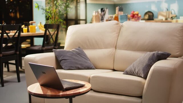 Empty living room open space with laptop on wooden coffee table. Couch and contemporary interior design create a modern atmosphere with no people in a rustic room with natural light and furniture.