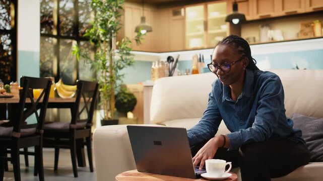 Adult woman works from home in cozy rustic living room using laptop for daily online tasks. Freelancer lifestyle includes remote work setup and natural light supporting productivity at home.