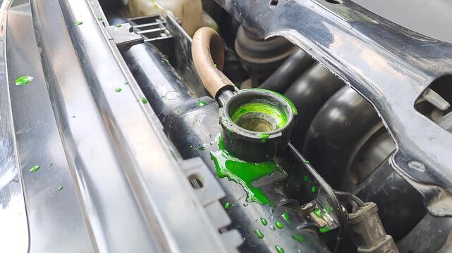 Close-up video footage of pouring bright green coolant into a car radiator reservoir tank. Automotive maintenance, engine service, and technology stock video.