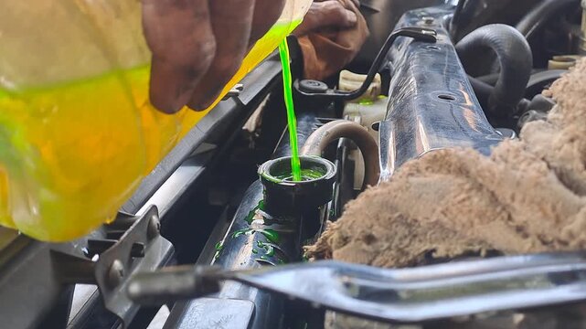 Close-up video footage of pouring bright green coolant into a car radiator reservoir tank. Automotive maintenance, engine service, and technology stock video.