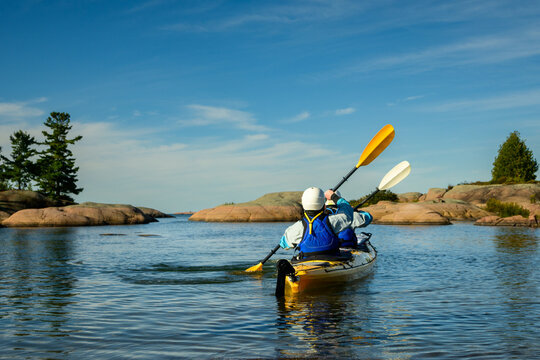 Two paddlers in a tandem kayak head out between pink granite islands in morning light with copy space on Georgian Bay, Ontario, Canada