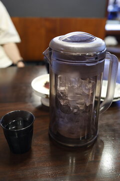 氷入りのお冷のピッチャーとコップ。飲食店の木製テーブル