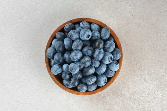 Fresh ripe blueberries in wooden bowl on a light gray textured background. Seasonal summer harvest, healthy food, natural nutrition, wholesome eating and nutritious source of vitamins and antioxidants