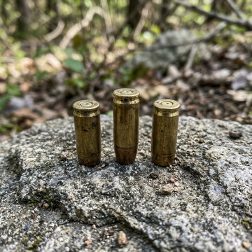 Three Brass Shell Casings Resting On A Textured Rock Surface Amidst Natural Forest Foliage