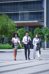 Two businesswomen and a young businessman in shirtsleeves coming down the plaza along an open pedestrian square, a conversation running as they walk, an informal business lifestyle frame © ultramansk