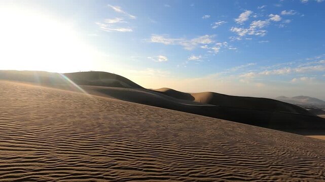 POV tracking shot speeding through vast desert sand dunes during golden hour under a bright blue sky.