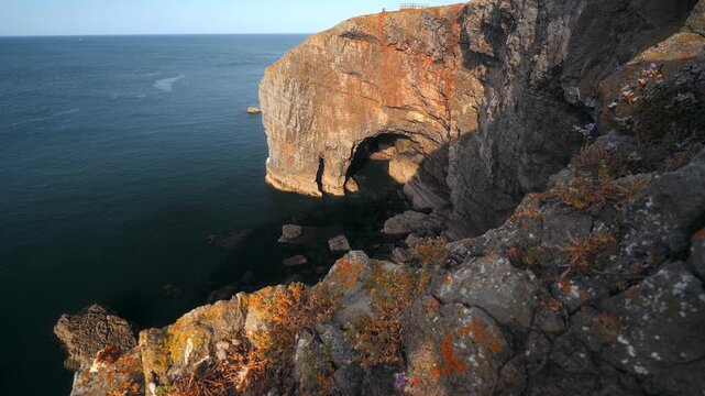 A limestone sea arch extends above dark blue water along the dramatic coastline of Pembrokeshire, Wales.