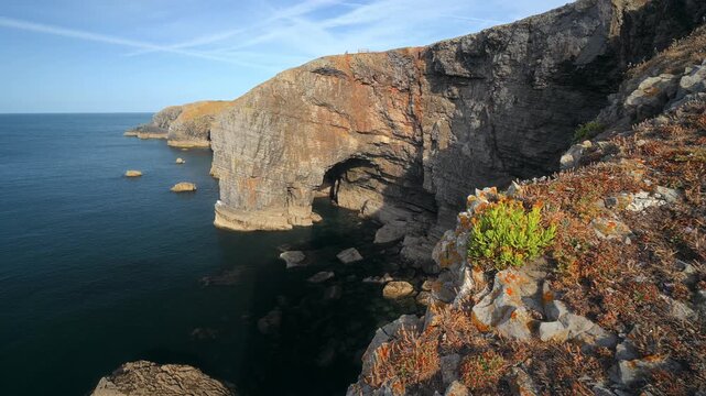 Rugged limestone cliffs feature a large natural sea arch above scattered shoreline rocks on the Pembrokeshire coast.