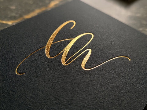 Gold foil calligraphy initial logo on black paper

Elegant gold foil handwritten script letter CA monogram on textured black paper. Luxury branding closeup. 