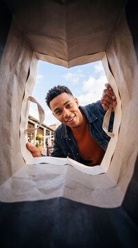 POV shot of a smiling man peeking inside a shopping bag, looking directly at the camera with excitement and anticipation, implying a delightful discovery.