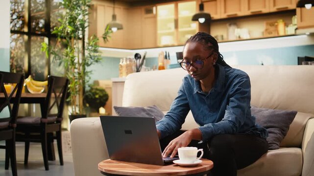 Young woman cracks knuckles from nervous habit while focused on laptop tasks at home, making repetitive popping sounds during telecommuting work.