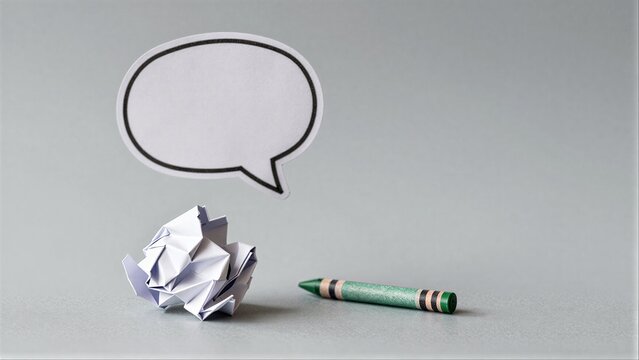 Crushed paper, green crayon, and speech bubble on plain gray surface.