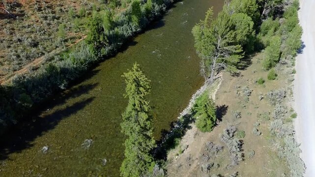 Aerial view of a river winding through forested terrain. Road runs parallel to the waterway. Trees line the riverbanks and slopes. Natural, quiet landscape with flowing river