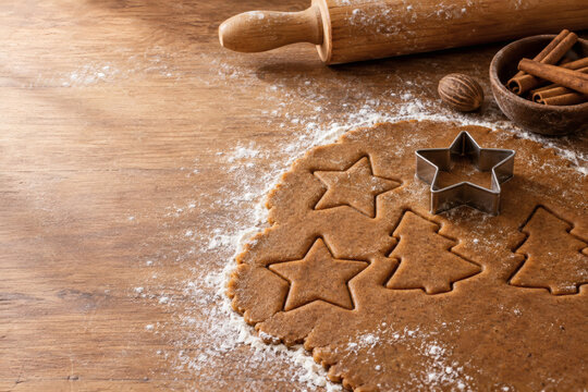 Rolled gingerbread cookie dough with star and tree shapes cut out, metal cookie cutter, rolling pin and cinnamon on a floured board