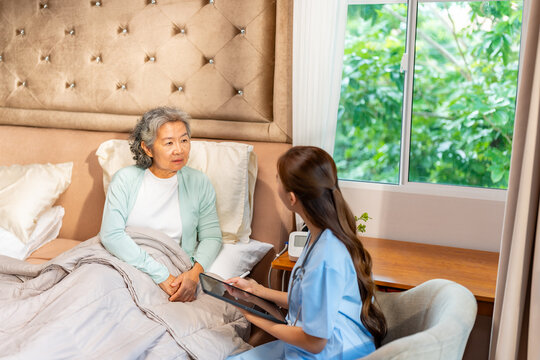 Asian female gerontological nurse visit senior woman patient at home, talking and using digital tablet health check, elderly care, home caregiver, medical healthcare consultation for healthy aging
