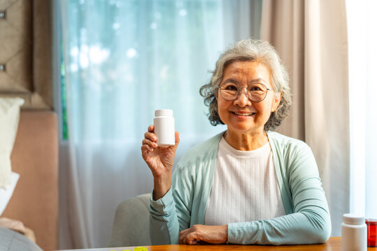 Portrait of Happy Asian senior woman holding medicine or vitamin supplements bottle. Smiling elderly patient showing medication, prescription drug, healthcare, treatment, wellness and healthy aging.