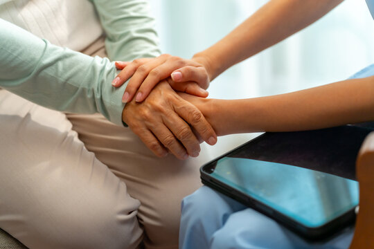 Female caregiver holding elderly woman hand for comfort and emotional support, senior healthcare assistance at home, compassion and trust in caregiving relationship, medical support and aging care.