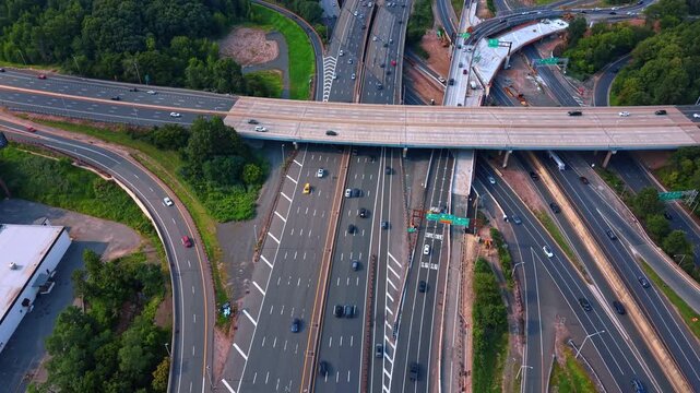 Approaching a massive concrete overpass slicing cleanly across a sprawling multi-lane interstate highway system. Busy motorways along thick patches of green forest near an industrial building.