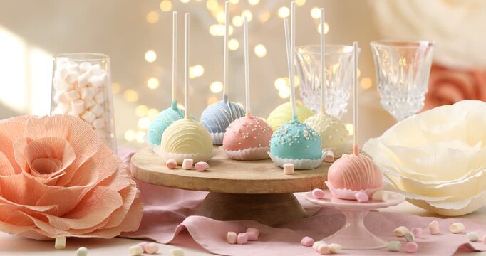 Woman putting tasty cake pops onto stand at white table against blurred lights, closeup