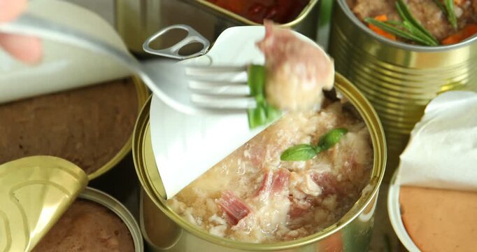 Woman eating canned meat with fork at table, closeup