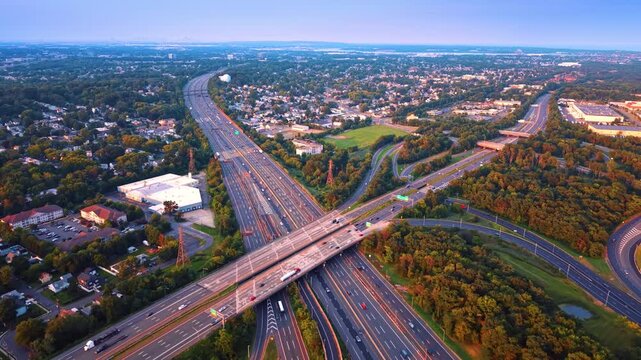 Vast highway junction where two major multi-lane interstates cross paths. Flat green landscape and city horizon with huge busy interchange.