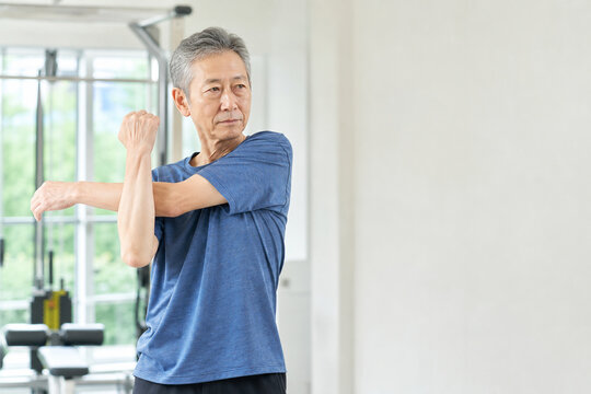 ジムで腕を伸ばしてストレッチする高齢男性